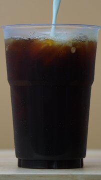 4K footage vertical video Front view Close-up plastic cup filled with iced coffee beautifully swirls with fresh milk.