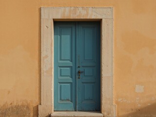 Fototapeta premium Vintage Turquoise Wooden Door Set Against a Textured Yellow Wall, Stone Frame.