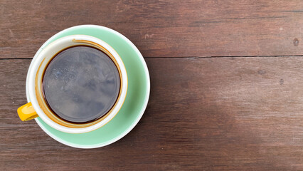 Top view of a colored coffee cup with frothy black coffee on a wooden surface