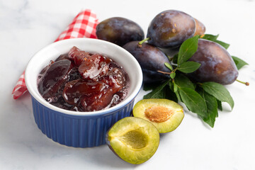 Homemade damson plum jam in blue ceramic bowl and berries on white wooden background.