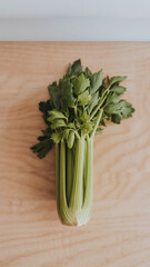 Upright celery displayed in glass vase on wooden background with warm indoor lighting