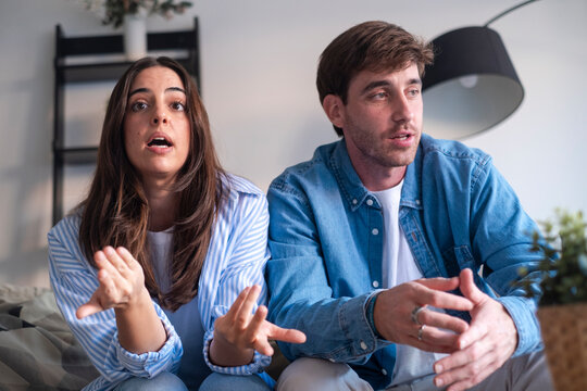 Couple sitting tensely on a sofa during a therapy session, facing serious relationship issues. Tension, emotional distance, addiction, trust concerns, and communication breakdown suggest deeper person