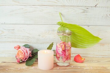 Spa still life with pink fresh roses flowers, candle and rose petal water, on wooden background....