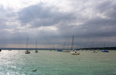 Lake scene with moored yachts, overcast weather, and gentle waves. Sunlight filtering through...