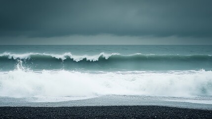 Dramatic ocean waves crashing on a dark sand beach under a stormy sky