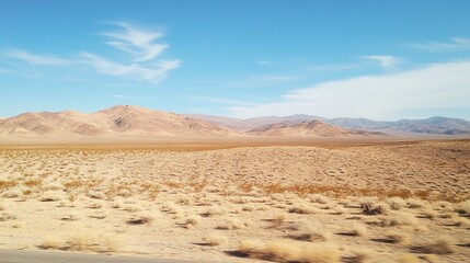 Expansive desert landscape under a clear blue sky, featuring arid terrain, sparse vegetation, and distant mountains