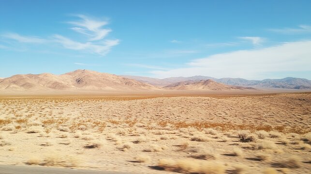 Expansive desert landscape under a clear blue sky, featuring arid terrain, sparse vegetation, and distant mountains