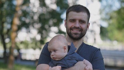 A father enjoys quality time with his baby in a park, surrounded by trees and natural light, reflecting a moment of joy and connection on a sunny day.