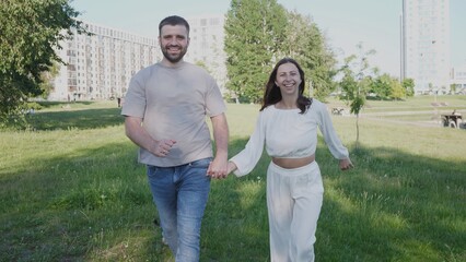 Joyful couple strolls together in a city park, enjoying the sunny weather and each other's company, with modern buildings visible in the background.