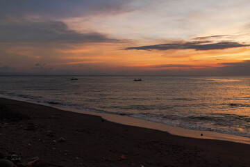 Dark sand beach meets the calm sea under a vibrant evening sky