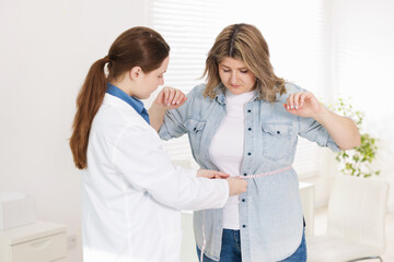 Weight loss. Nutritionist measuring overweight woman's waist with tape in clinic