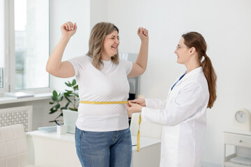 Fototapeta premium Weight loss. Nutritionist measuring happy overweight woman's waist with tape in clinic