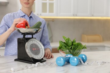 Woman weighting vegetables on kitchen scale at white marble table indoors, closeup