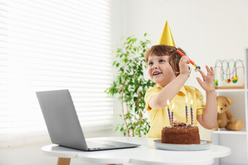 Birthday celebration. Little boy with cake having video call via laptop at table indoors. Space for...
