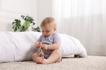 Cute little baby playing with rattle on floor indoors