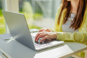 Cropped hands of businesswoman typing on laptop at office desk. Modern workplace, technology and professional lifestyle concept. Independent woman typing on laptop in coworking space.