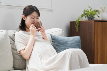 ソファーで飲み物を飲む妊婦　ライフスタイルイメージ