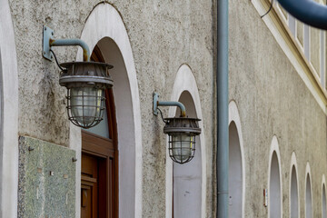 building facade with arched niches and industrial-style metal wall lamps. Gray plastered wall with architectural details