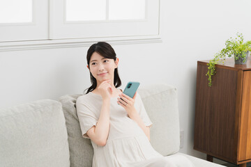ソファーでスマートフォンを操作する妊婦　ライフスタイルイメージ