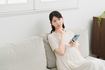 ソファーでスマートフォンを操作する妊婦　ライフスタイルイメージ