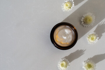 Jar of cosmetic cream on stone table decorated with flowers. Beauty, spa and skincare lifestyle aesthetic concept top view.