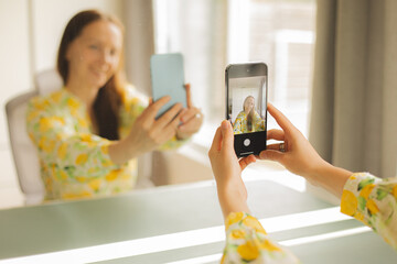 Young woman wearing a white dress with a lemon print taking a selfie with her smartphone. POV shot...