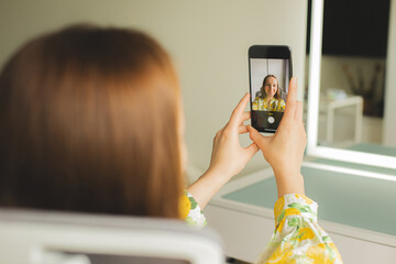 Young woman wearing a white dress with a lemon print taking a selfie with her smartphone. POV shot...