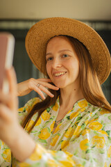 Young woman wearing a white dress with a lemon print taking a selfie with her smartphone. POV shot...