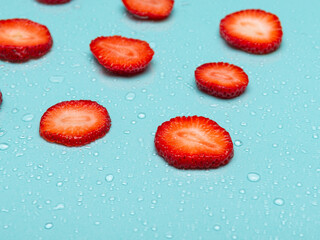 Fresh strawberry slices arranged on a light blue surface, glistening with water droplets