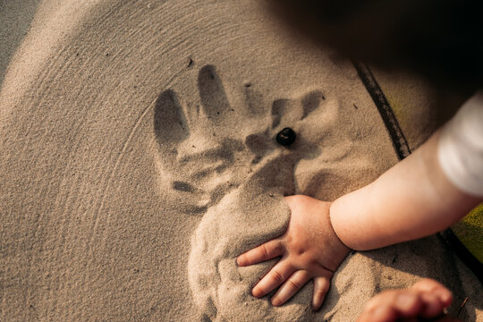 A close view of a young girl drawing in the sand with a stick during golden hour, capturing childhood creativity and nature