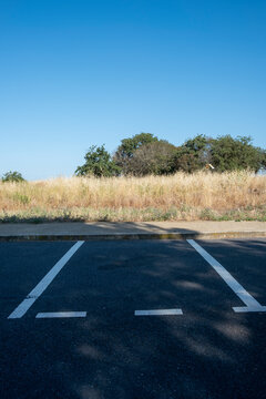 Abandoned parking area with dry vegetation and asphalt lines under blue sky, representing emptiness and future urban transitions