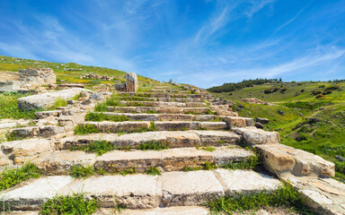 Ancient stone stairs leading uphill through Hierapolis archaeological site, Turkey. Steps covered with grass, surrounded by green hills, under clear blue sky. UNESCO World Heritage Site near Pamukkale