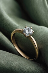 Elegant gold engagement ring with sparkling diamond resting on green silk, symbolizing luxury, romance, commitment and timeless beauty in close-up detail.