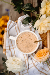 Golden spoon stirs creamy latte in white cup, surrounded by blooming roses. Rustic summer aesthetic with floral charm.
