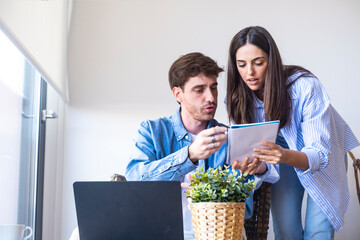 Young couple sitting at a desk at home discussing their family budget. Focused expressions while...