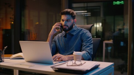 Businessman Indian guy multitasking business man male in night late office overtime work talking mobile phone call discuss computer laptop commerce smartphone conversation smiling manager consulting