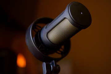 Close-up of a professional condenser microphone in a shock mount against a dark background with warm bokeh highlights. Photo. Selective focusing. High resolution