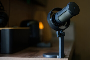 Close-up of a microphone on a desk in a dark home studio environment with blurred background suggesting podcasting or streaming setup. Photo. Selective focusing. High resolution