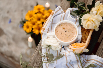 Hot latte in a mug with golden spoon, lying on rustic linen surrounded by soft roses. Gentle and...