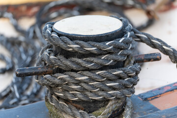 Coiled marine rope wrapped around a wooden bollard on a dock, highlighting braided texture and...