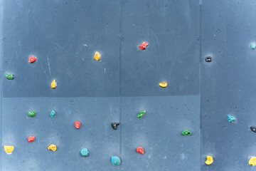 A wide shot of an outdoor climbing wall with multicolored grips mounted on a gray surface. Designed...