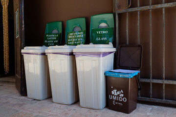 Four recyclable trash cans for glass, plastic and food are neatly arranged in a row against a wall,...