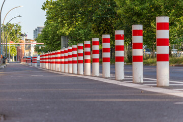 White bollards with red stripes stand in a straight line along a street. This photo shows an urban traffic feature in sunlight.