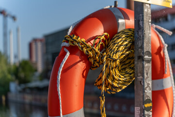 An orange lifebuoy with a yellow rope is attached to a post. The scene depicts safety precautions on the water.