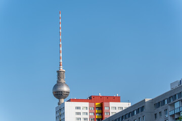 The Berlin TV Tower rises above colorful prefabricated buildings into the clear sky. The combination of modern technology and residential architecture symbolizes the city s development.