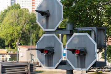 A special waterway traffic light with red signals stands against a green background. The technical device appears industrial and unusual in the context of the cityscape