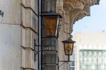 Two ornately decorated wall lanterns adorn an old facade in Berlin. The lanterns create a nostalgic charm and are reminiscent of classic urban furniture.