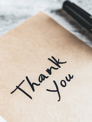 Handwritten thank you note on brown paper with pen