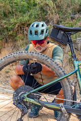 vertical Senior cyclist inflating tire of electric mountain bike on a trail
