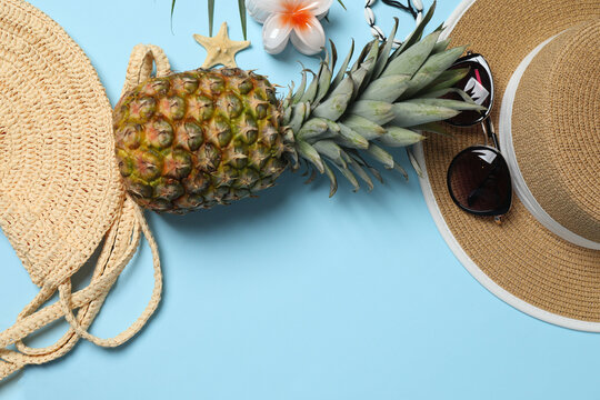 Tropical vibes shot from above. Straw hat, sunglasses, pineapple, wicker bag, beach accessories on a blue background. Perfect for advertising or text overlays